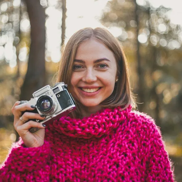 Smiling woman in a magenta scarf holding a camera